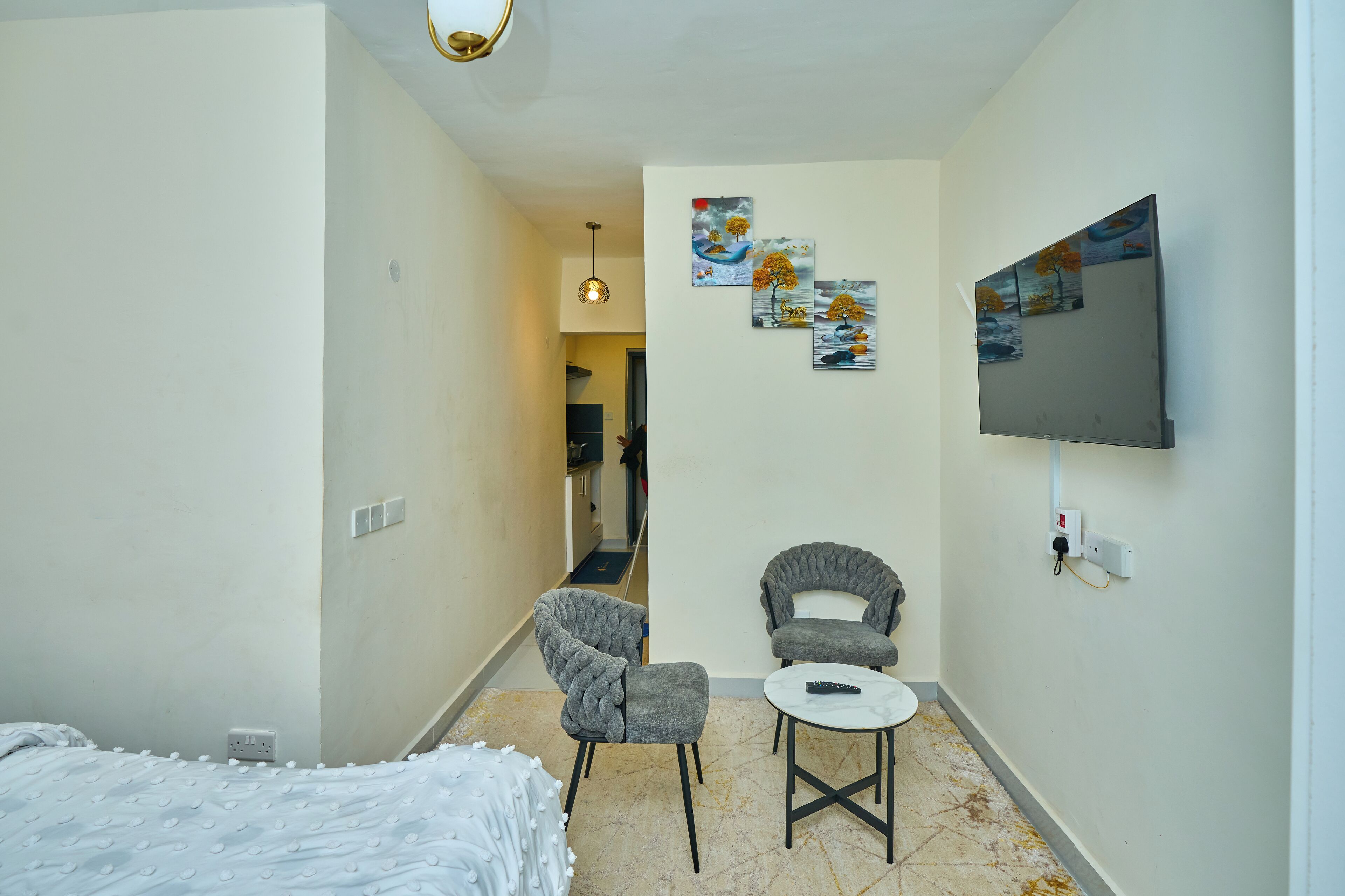 Habitación de hotel con cama, dos sillones, una mesita, televisor montado en la pared y cuadros decorativos.