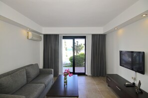 A modern living room with a sofa, a coffee table with flowers, a flat-screen TV, and a sliding glass door leading to a balcony.