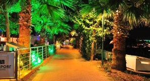 A pathway lined with palm trees and illuminated by green lights, leading to a building with a sign that reads "PORT HOTEL".