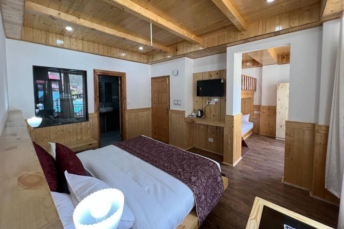 A wooden-paneled room with a bed, a desk, a TV, and a bathroom visible through an open door.