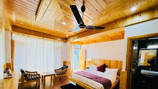 A wooden-paneled room with a bed, a desk, chairs, and a ceiling fan. - Hotel Sakura Palace (Manali)