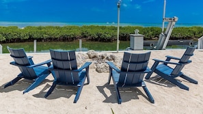 Four blue Adirondack chairs facing a beach with clear blue water and a rocky shoreline. - The Katch on the Ocean in Duck Key w/ Pool and loads of privacy 2 kayaks included (Marathon)