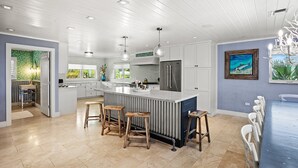 Una cocina moderna con una isla central, taburetes de bar y una zona de comedor con una mesa azul.