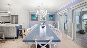 A spacious kitchen with a long dining table, white chairs, and a chandelier. - The Katch on the Ocean in Duck Key w/ Pool and loads of privacy 2 kayaks included (Marathon)