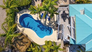 An aerial view of a resort with a swimming pool, palm trees, and a blue-roofed building.