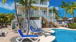 A poolside area with lounge chairs, a pool, and a multi-story building with balconies.