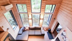 A cozy cabin interior with a large windowed seating area, wooden walls, and a view of the forest.