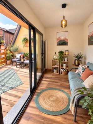 A modern living room with a sofa, a dining area, and a view through a glass door to an outdoor patio.