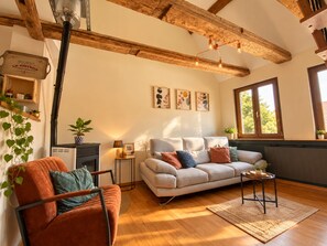A cozy living room with a sofa, a chair, a coffee table, and a fireplace. There are framed pictures on the wall and a window with a view.