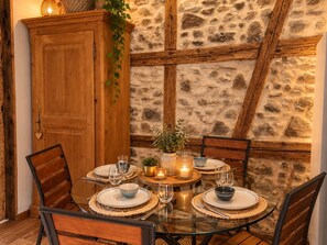 A dining area with a stone wall, wooden beams, and a glass table set for four.