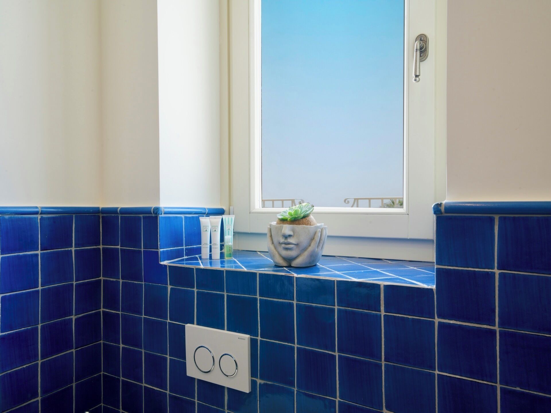 Ein Badezimmer mit blauen Fliesen, einem Fenster und einer Pflanze in einem Keramiktopf.