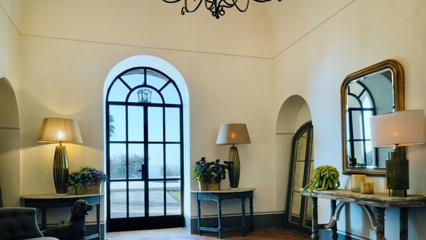 A spacious room with a large arched window, a dog statue, two lamps, a mirror, and a rustic console table. - Villa Gialisa (Sorrento)