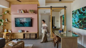 A modern living room with a large flat-screen TV, a dining area with a glass table, and a hallway leading to another room.