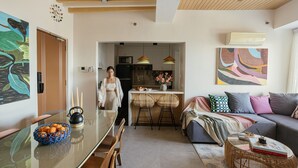 A modern living room with a sofa, a dining table with chairs, and a kitchen area in the background.