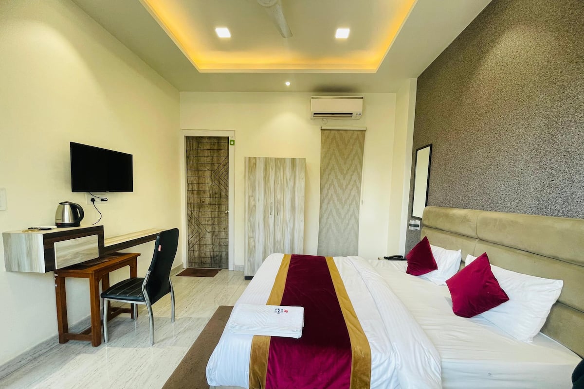 Habitación de hotel con cama, escritorio, silla, televisor y aire acondicionado.
