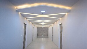 A long, narrow hallway with a modern ceiling design featuring recessed lighting and a central light fixture. - Hotel Kapson Palace (Bareilly)
