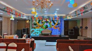 A banquet hall with a stage, red upholstered chairs, and a chandelier. - Hotel Kapson Palace (Bareilly)