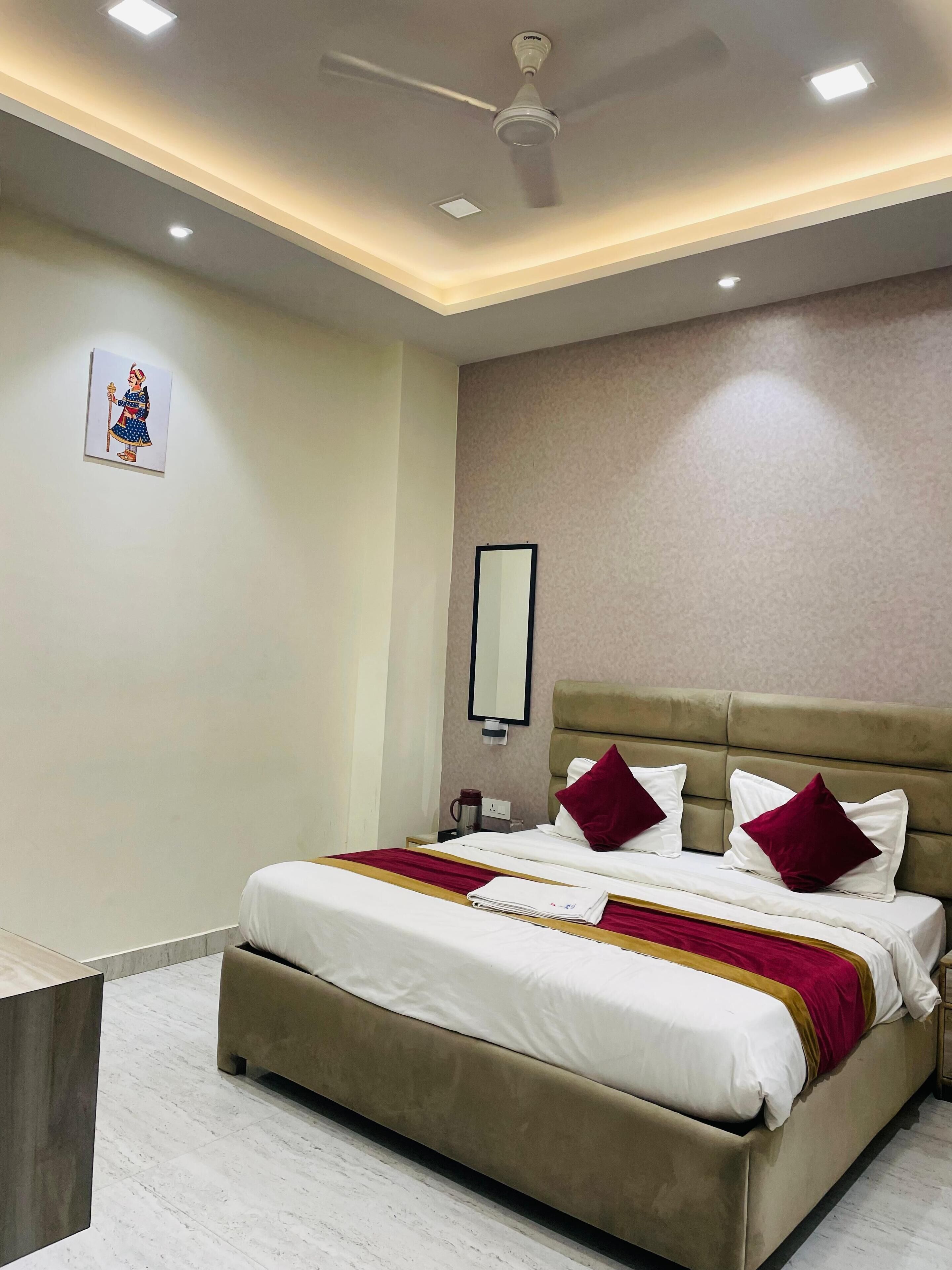 Una habitación de hotel con una cama grande, un ventilador de techo, iluminación empotrada, una mesita de noche, un espejo y una obra de arte colgada en la pared.