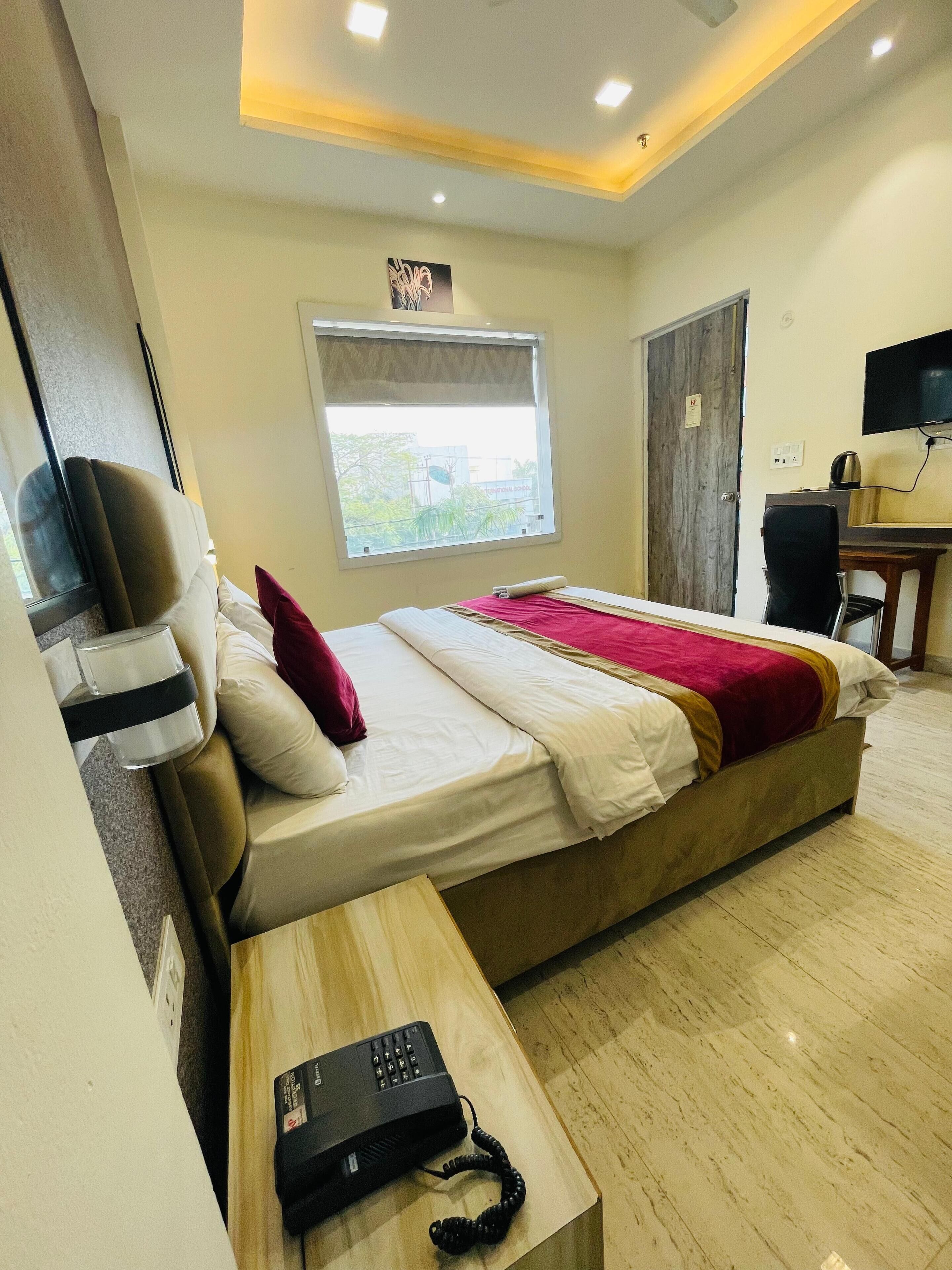 A hotel room with a bed, a desk with a telephone, a television, and a window with a view of greenery.