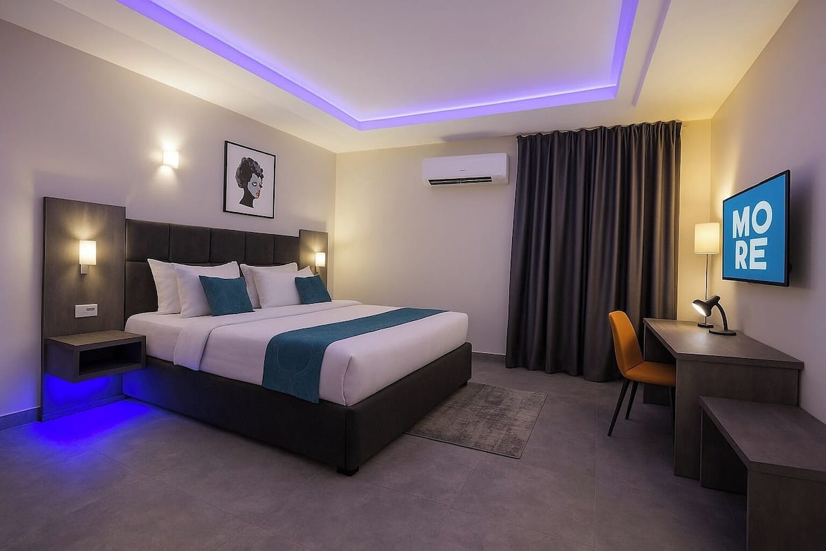Una camera d'albergo moderna con un letto, comodini, una scrivania, una sedia, un condizionatore d'aria e un poster motivazionale.