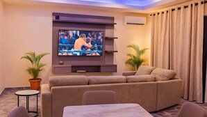 Una sala de estar con televisor en la pared, un sofá, una mesita de mármol y dos plantas en macetas.
