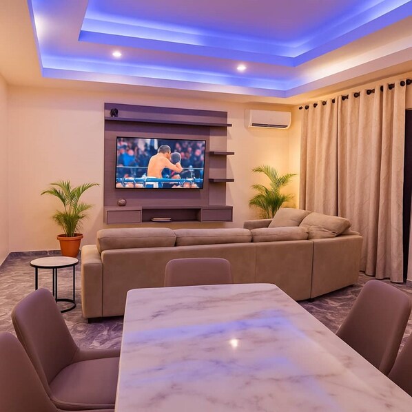 A living room with a TV mounted on the wall, a sofa, a marble table, and two potted plants. - 154 Apartment & Hotels (Abuja)