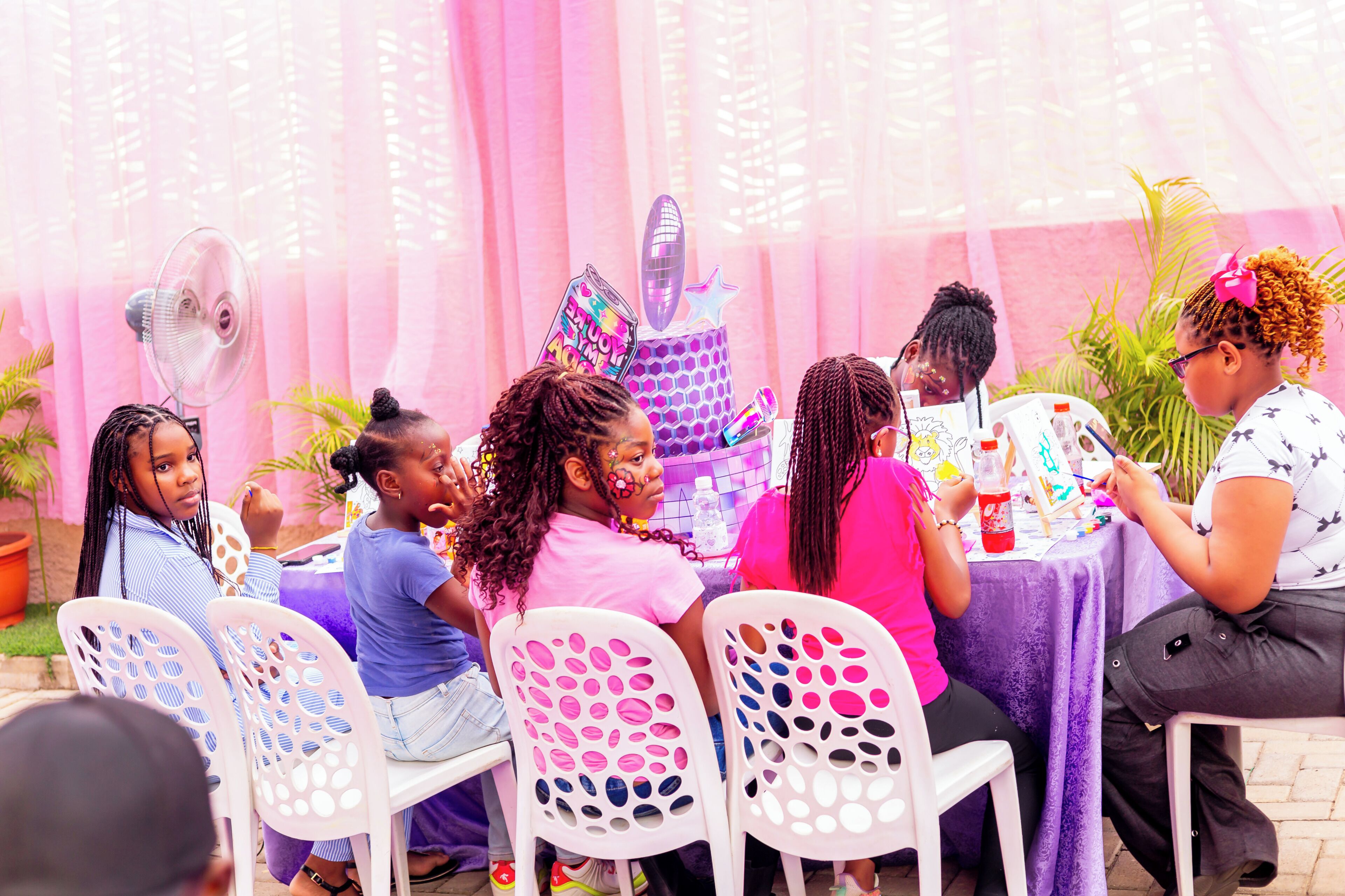 A group of people seated at a table with a purple tablecloth, engaged in an activity with various items on the table.