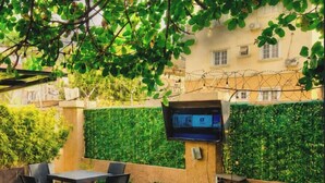 Un patio exterior con una pantalla de televisión, asientos al aire libre y una pared verde.