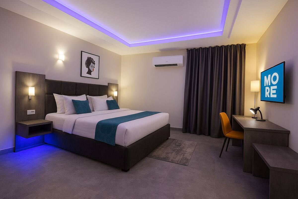 Una moderna camera d'hotel con un letto, comodini, una scrivania, una sedia, una TV e un condizionatore d'aria.