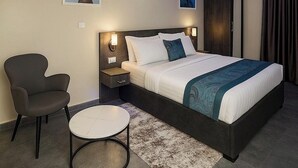 Una habitación de hotel con cama, mesita de noche, silla y obras de arte en las paredes.