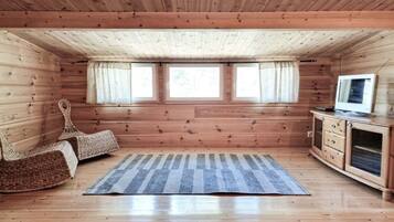 A wooden cabin room with a large window, a television, and a woven chair.