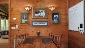 L’intérieur d’un chalet en bois comprend une table à manger, des tableaux encadrés et un tableau blanc sur lequel est inscrit un message de bienvenue.