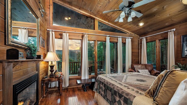 Une chambre confortable dans un chalet, avec une cheminée, un grand lit et vue sur la forêt.