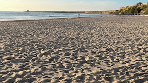 Une vaste plage de sable fin, avec un ciel dégagé et une mer calme.