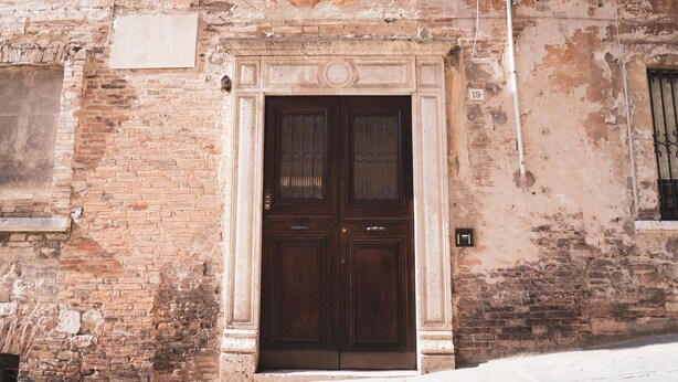 A weathered brick building with a large, dark wooden door.