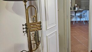A brass table lamp with a grey shade on a wooden table, a white door, and a dining area visible through an open door.