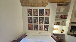 A large bed with white linens and towels, a brick wall, and a bookshelf with books.