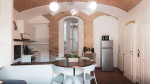 A compact kitchen with a central island, white chairs, and a brick archway.