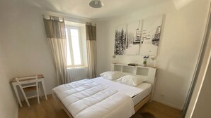 A bedroom with a large bed, a small table, a radiator, and a window with curtains.