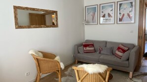 A living room with a grey sofa, two wicker chairs, a cowhide rug, a hanging light fixture, and three framed pictures on the wall.
