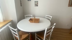 A round white table with four white chairs, a wooden tray, and three small wall decorations.