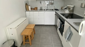 A modern kitchen with white cabinets, a wooden table, and a trash bin.