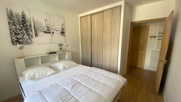 A bedroom with a bed, a wardrobe, a desk with a lamp, and wall art.
