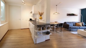 Uma cozinha moderna com uma ilha central, uma sala de jantar com mesa e cadeiras, e uma sala de estar com sofá e mesinha de centro.