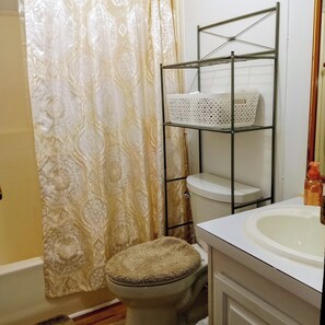 Une salle de bain comprenant des toilettes, un lavabo, une étagère en métal et un rideau de douche à motifs.