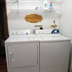 Een wasmachine en droger met bedieningspanelen, een houten plaquette erboven en een plank met schoonmaakmiddelen.