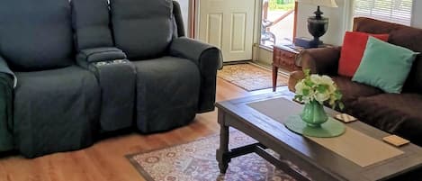 Ett vardagsrum med en soffa, ett soffbord och en matta. Det finns en dörr som leder ut.