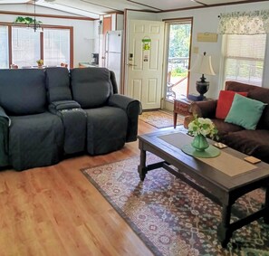 A living room with a sofa, a coffee table, and a rug. There is a door leading outside.