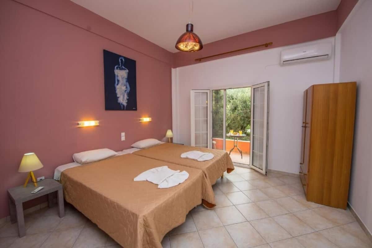 A hotel room with two beds, a large window, an air conditioning unit, and a wooden wardrobe.