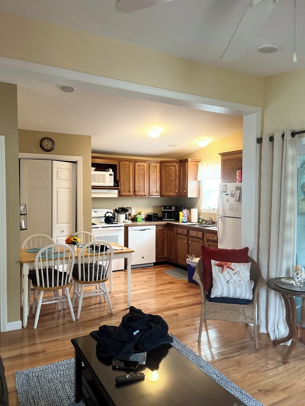 A kitchen with wooden cabinets, a dishwasher, and a microwave. There is a dining area with a table and chairs. - Charming 2-bedroom cottage with all the amenities you need! (Wells)